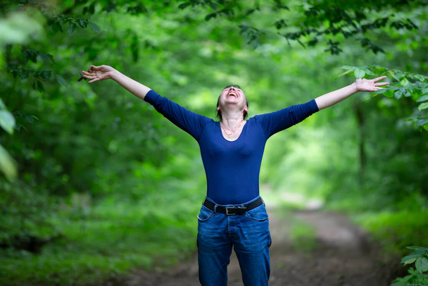 Onnellinen keski-ikäinen nainen levittää kätensä metsään. - Valokuva, kuva