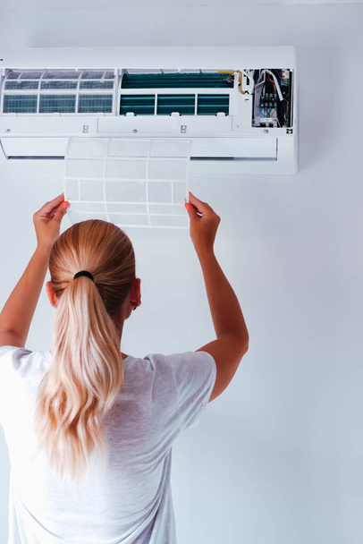 Repair service of the air conditioner. The woman removes the air conditioner filter. Back view. Filter of air conditioner in female hands. - Foto, Imagem
