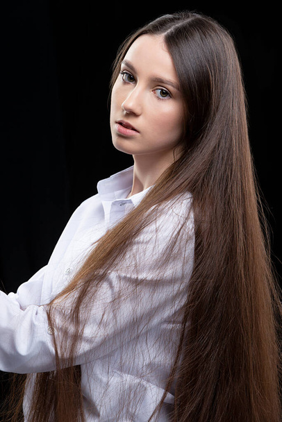 Stüdyoda gri arka planda poz veren uzun düz saçlı, beyaz gömlekli güzel bir genç kız. - Fotoğraf, Görsel