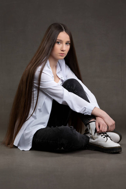 Schöne brünette Mädchen mit sehr langen Haaren auf einem grauen Hintergrund. - Foto, Bild