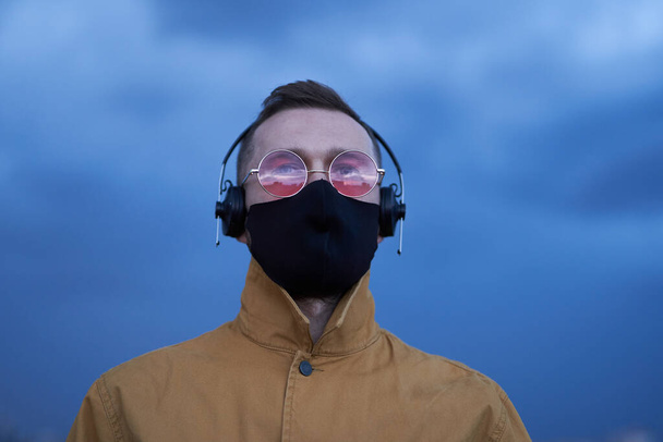 Άντρας με γυαλιά ηλίου και μαύρη μάσκα προσώπου ακούγοντας μουσική - Φωτογραφία, εικόνα