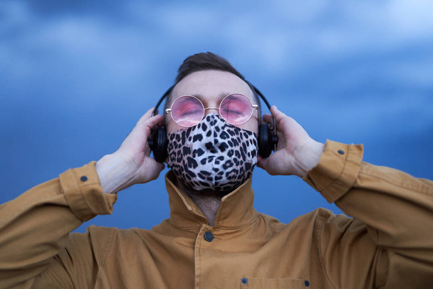 Hombre con gafas de sol y máscara de patrón de leopardo escuchando música - Foto, imagen