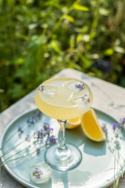 Pompadour Glas Lavendellimonade mit Würfeleis mit Lavendelblüten. Tisch im Sommergarten. - Foto, Bild