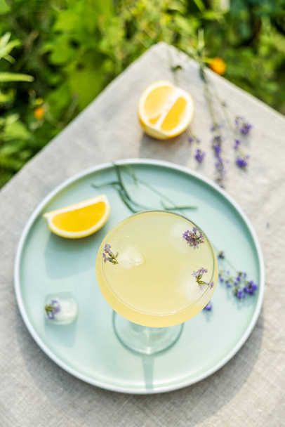 Top view Pompadour glass of lavender lemonade with cube ice with lavender flowers. Table in summer garden. - Photo, Image