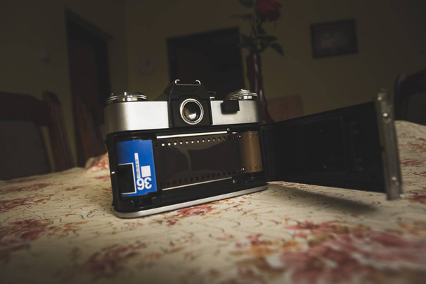 家のテーブルの上には古いアナログカメラが置かれている. カメラは背面に開いているので,写真のフィルムを見ることができます. - 写真・画像