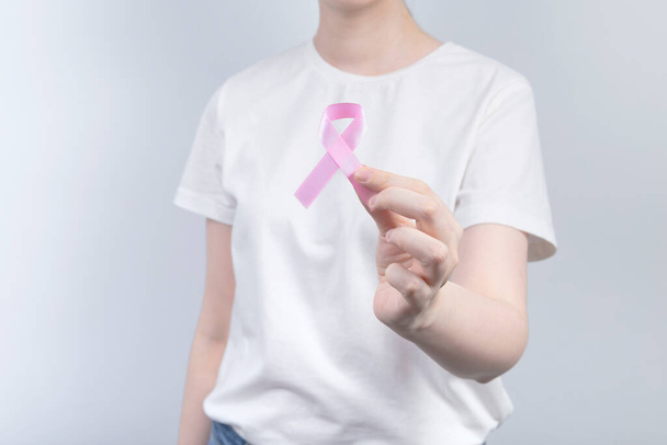 World Breast cancer day concept. Woman in white T-shirt holds pink ribbon in her hand. October Breast Cancer Awareness month - Foto, Bild