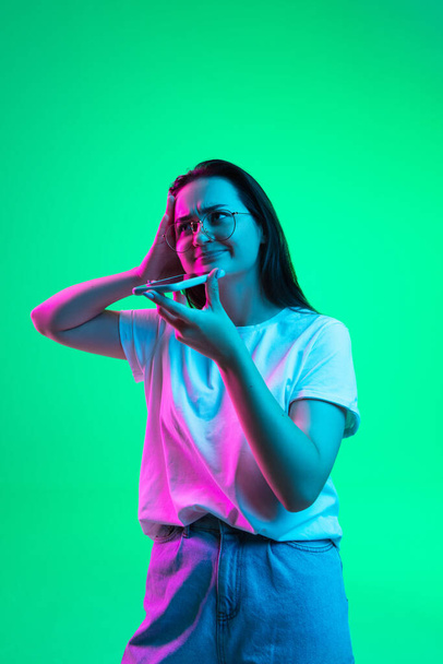 Demi-dixième portrait de jeune belle fille, modèle féminin en lunettes avec smartphone isolé sur fond vert au néon. - Photo, image