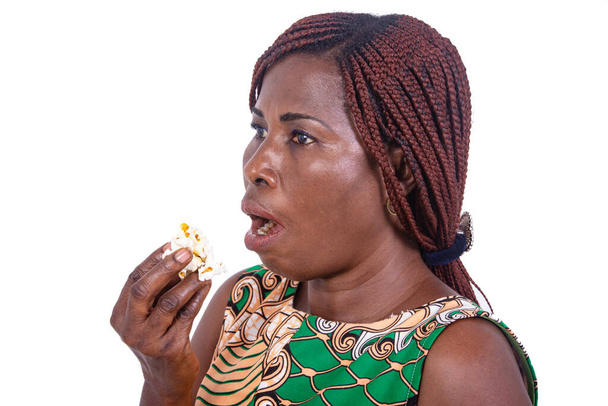 Gecelik peştamallı güzel bir kadın beyaz bir arka planda durmuş patlamış mısır yiyor.. - Fotoğraf, Görsel
