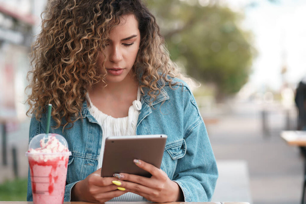 Latin woman using a digital tablet while sitting at a coffee shop outdoors. - Φωτογραφία, εικόνα