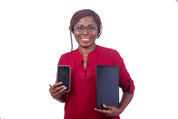 hermosa mujer de negocios en gafas de pie sobre fondo blanco presentando una tableta y teléfono celular sonriendo. - Foto, imagen