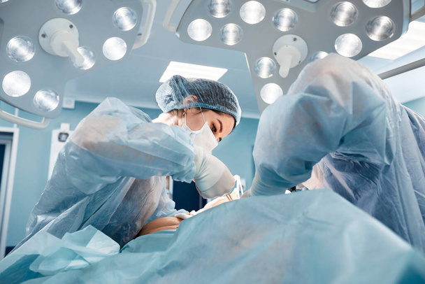 手術台の手術中に外科医の男性と女性が1つのチームで、近代的な機器の医師は腫瘍学的手術を行います - 写真・画像