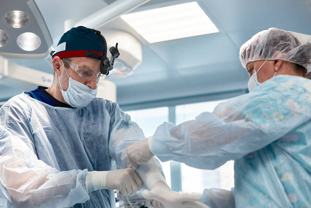 Mains de médecins en gants pendant une opération, gros plan d'une infirmière opératrice aidant un chirurgien à mettre des gants de styryl avant l'opération. - Photo, image