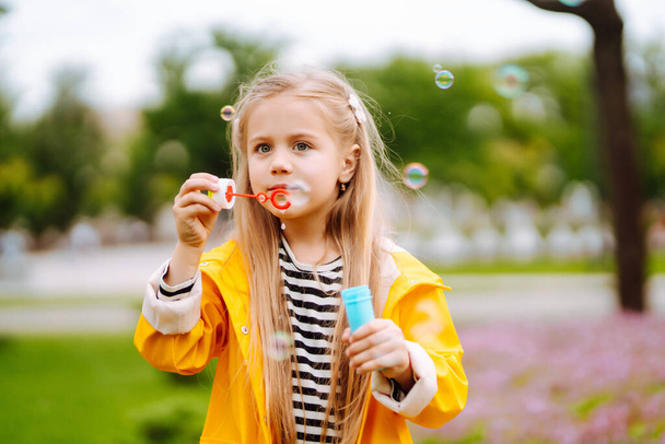 Little adorable girl blowing soap bubbles outdoors in summer park. Happy childhood concept. - Photo, Image