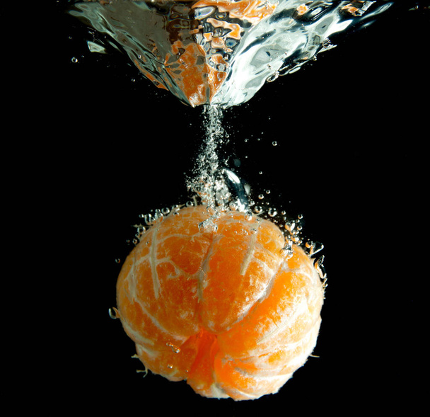 mandarijn die in het water valt, geïsoleerd op een zwarte achtergrond - Foto, afbeelding