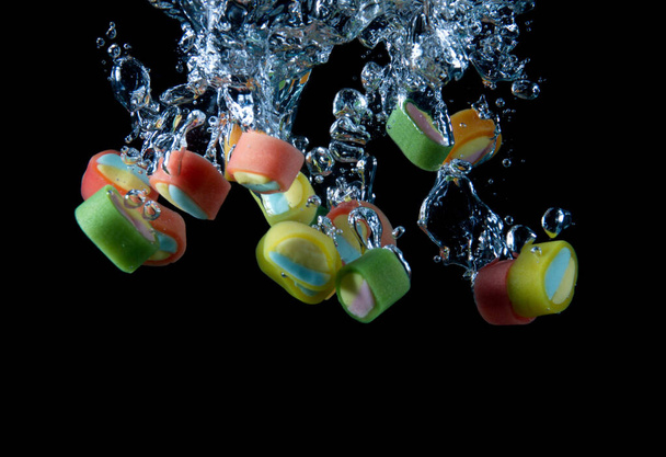 close-up view of multicolored candies falling into water on black background - Fotografie, Obrázek