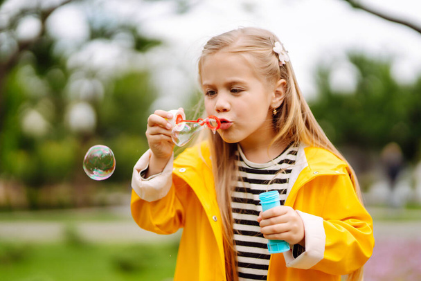Little adorable girl blowing soap bubbles outdoors in summer park. Happy childhood concept. - Fotó, kép