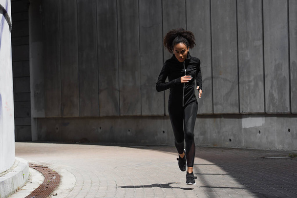 Jeune femme afro-américaine regardant la caméra tout en faisant du jogging dans la rue urbaine  - Photo, image