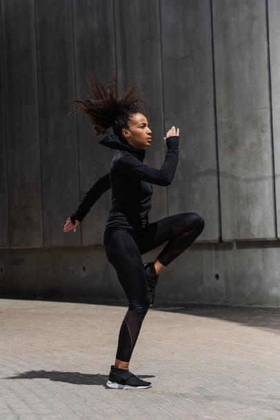 Side view of african american sportswoman warming up on urban street  - Photo, Image