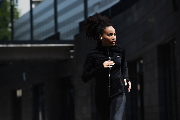 African american woman in earphone jogging on urban street  - 写真・画像
