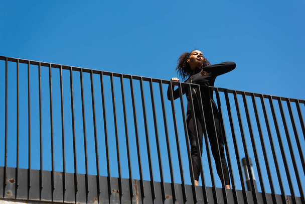 Nízký úhel pohledu na africké americké sportovkyně ve sluchátku strečink na mostě  - Fotografie, Obrázek
