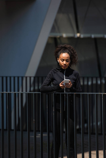 Afrikai amerikai sportos nő fülhallgatóban okostelefonnal a szabadban  - Fotó, kép
