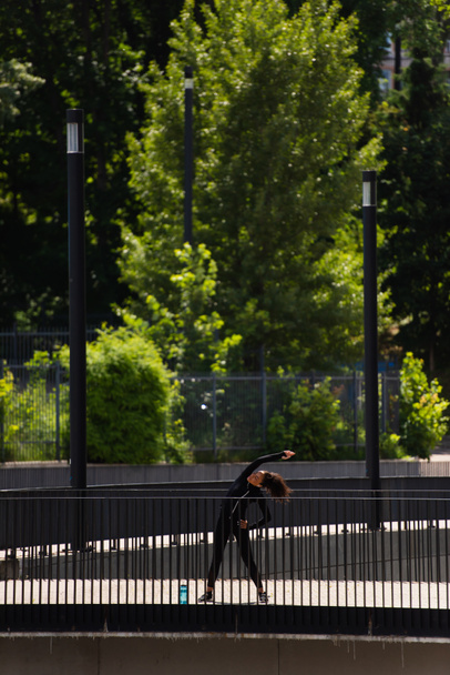 Young african american sportswoman bending while training on bridge  - Foto, afbeelding