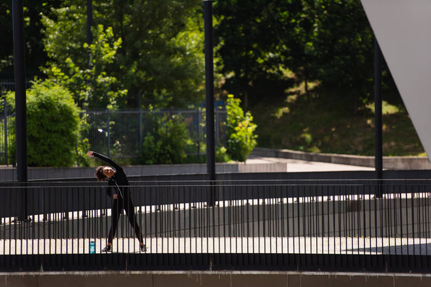 Femme sportive afro-américaine travaillant près d'une bouteille de sport sur un pont  - Photo, image