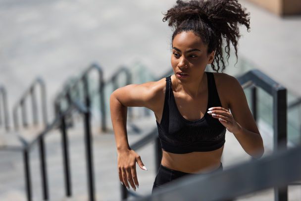 Pretty african american sportswoman running on blurred stairs  - Photo, Image