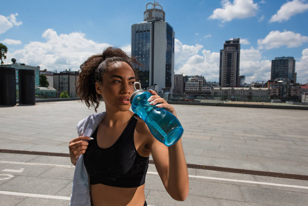 Africká americká sportovkyně drží ručník a pitnou vodu venku  - Fotografie, Obrázek