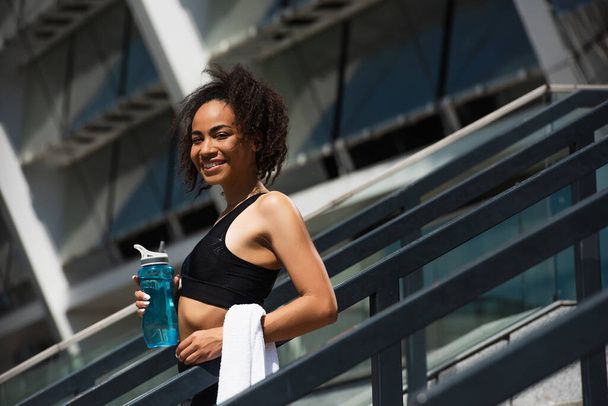 African american sportswoman with towel and water smiling at camera outdoors  - Foto, Imagem