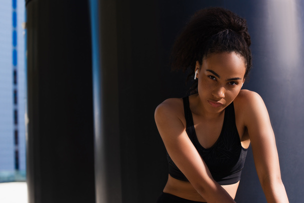 African american sportswoman in earphone and black top looking at camera outdoors  - Photo, Image