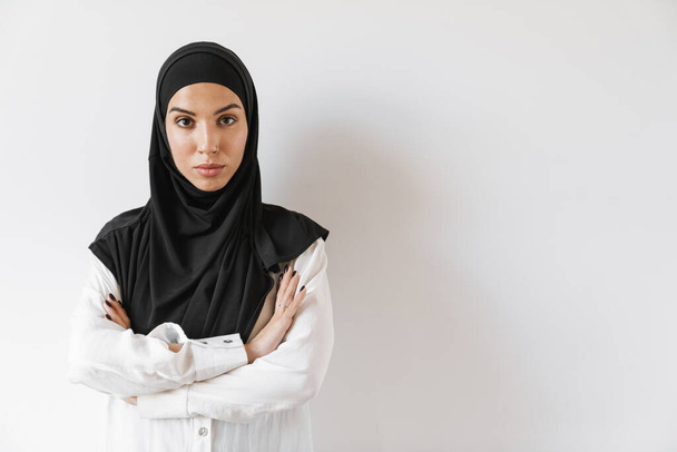 Een zelfverzekerde moslim vrouw met doorboorde neus staande met gekruiste armen in de witte studio - Foto, afbeelding