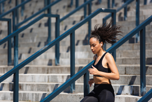 Fit african american sportswoman in earphone running on stairs  - Фото, зображення
