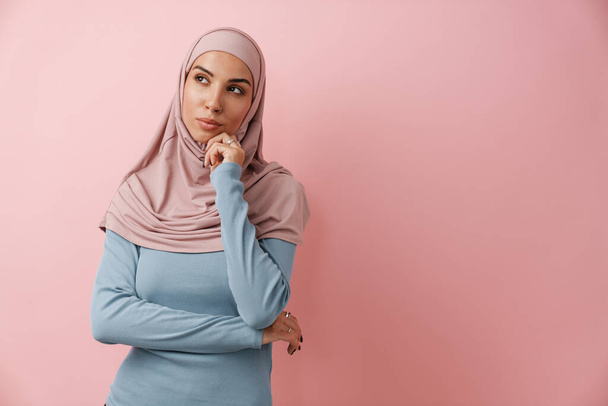 Mietteliäs musliminainen vaaleanpunaisessa hijabissa katsoo pinkkiin studioon. - Valokuva, kuva