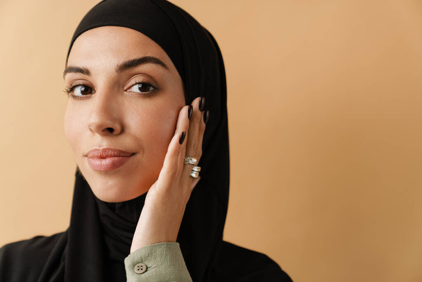 Ein Porträt der selbstbewussten muslimischen Frau mit schwarzem Hijab und die Hände vor dem Gesicht im orangefarbenen Studio - Foto, Bild