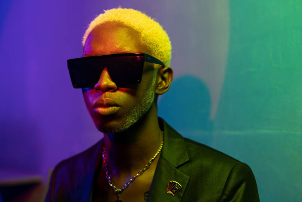 Portrait photo of a dark-skinned guy with blond hair. Dressed in a black jacket and sunglasses. With metal ornaments around his neck - Photo, image