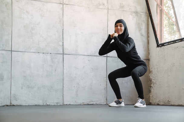 Young muslim woman in hijab doing exercise while working out indoors - Foto, Bild