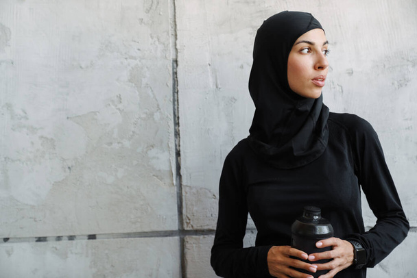 Young muslim woman in hijab standing with water bottle indoors - Photo, Image