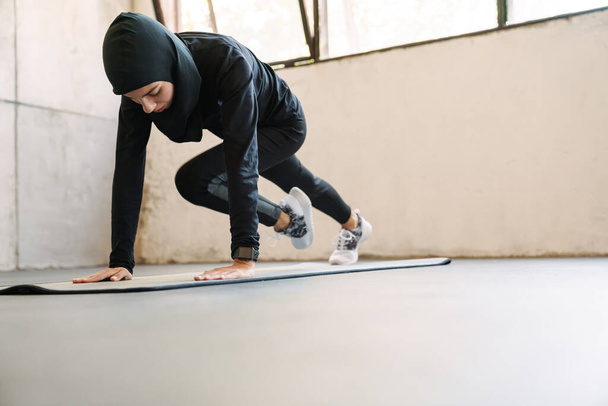 Young muslim woman in hijab doing exercise while working out indoors - Photo, Image