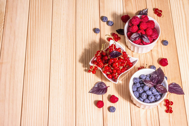 Assorted ripe berries in bowls. Fresh raspberries, blueberries, and red currants. Wooden boards table, top view - Photo, Image