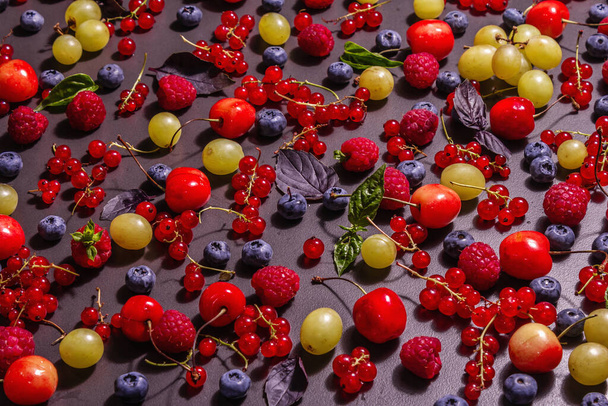 Assorted ripe berries, scattered on a black stone background. Fresh raspberries, blueberries, grape, sweet cherries, and red currants. A modern hard light, dark shadow, place for text - Photo, Image