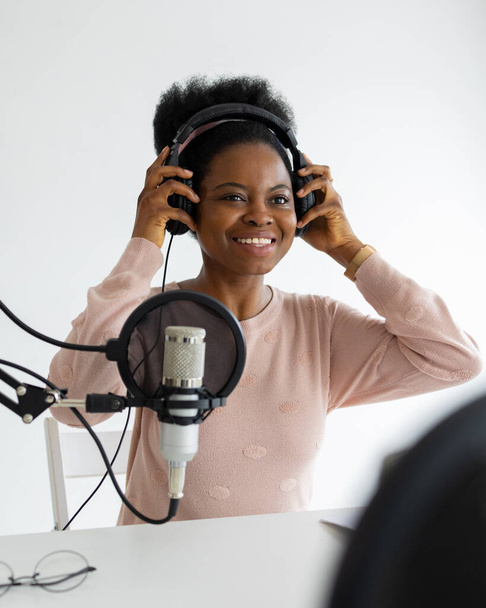 African American woman with headphones and a microphone recording a podcast in a recording studio - Valokuva, kuva