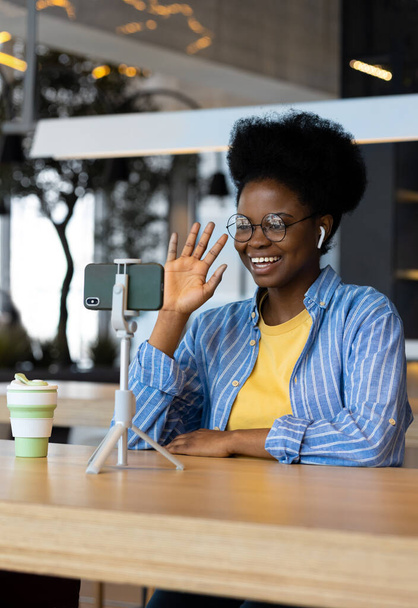 millennial African American woman in a public place watching a webinar or chatting on a webcam from her smartphone - Foto, Bild