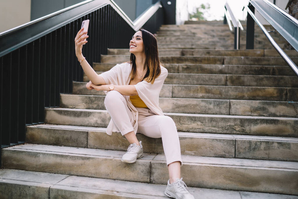 Toothy hipster girl shooting influence vlog during travelling time for creating funny content, happy Caucasian blogger smiling at front camera for clicking positive selfie images via mobile app - 写真・画像
