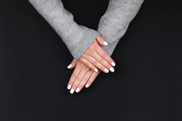 Female hands in gray knitted sweater with beautiful manicure - white nails on black background, banner with copy space. Nail care concept - Фото, зображення