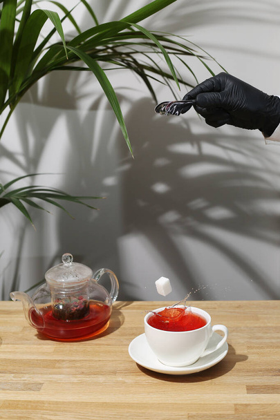 ref fruit tea on wooden table. sugar cube falling in cup. splash of tea. tea pot with fruit tea. - Photo, Image