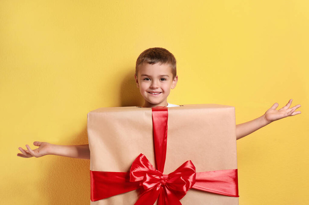 Cute little boy dressed as gift box on yellow background. Christmas suit - Foto, Imagen
