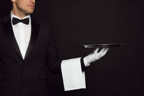 Butler with tray on black background, closeup - Zdjęcie, obraz