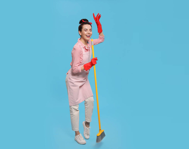 Young housewife with broom having fun on light blue background - Zdjęcie, obraz