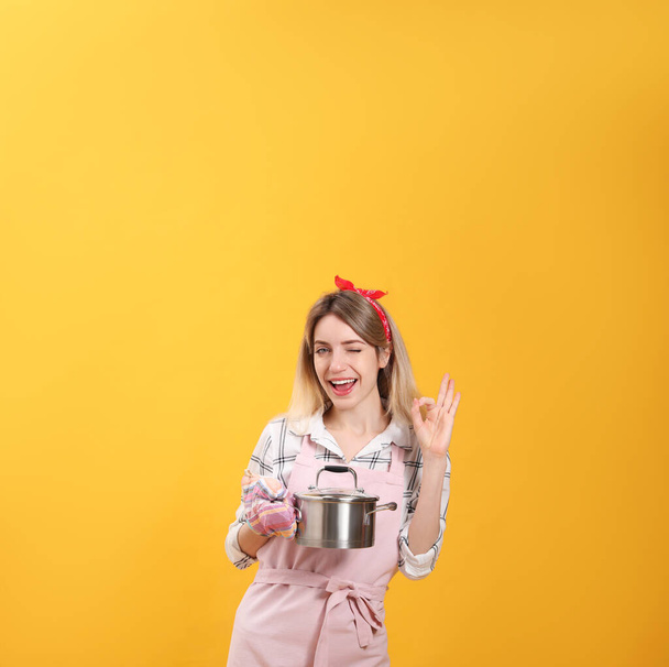 Young housewife with pot on yellow background - Foto, Imagem